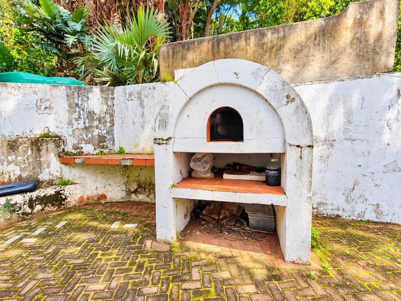 Outdoor patio area featuring a built-in masonry pizza oven, brick paving, and a retaining wall, requiring maintenance and cosmetic updates.