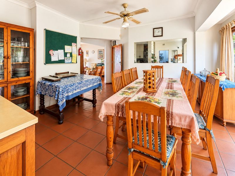 Spacious dining room featuring terracotta floor tiles, a ceiling fan, and a convenient pass-through window connecting to the kitchen area.