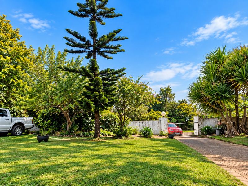 A well-maintained front garden featuring a paved driveway, established trees, and a secure gated entrance with a boundary wall.