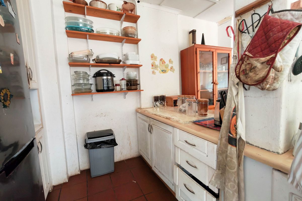 A compact kitchen featuring built-in cabinetry, open shelving, and tiled flooring, currently showing signs of wear and requiring cosmetic updates.