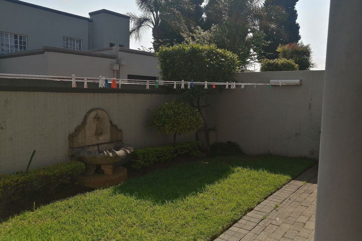 A private rear garden area featuring a paved walkway, a small lawn, and a decorative stone water feature against a boundary wall.