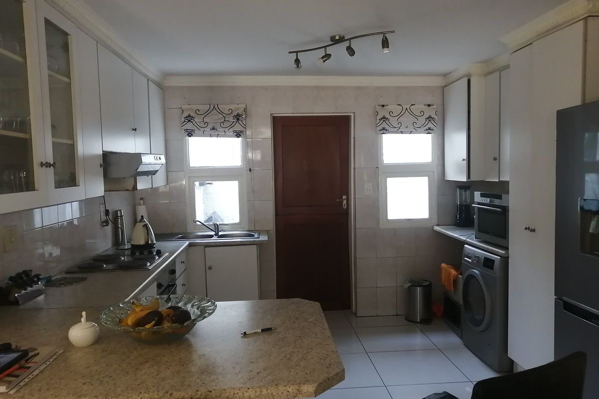 Functional kitchen featuring white cabinetry, laminate countertops, tiled backsplash, and integrated appliances, offering a practical layout with direct access to an exterior door.