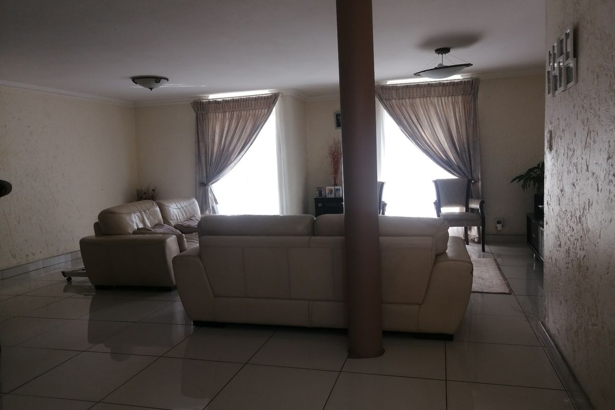 Spacious living area featuring large format floor tiles, a central structural column, and natural light through dual window sets.