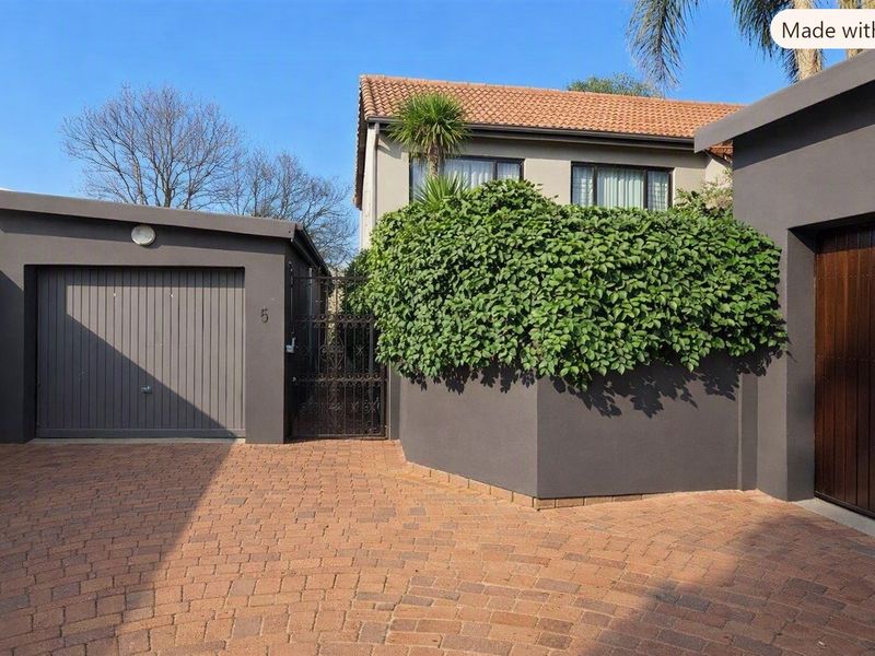Front exterior view of the townhouse featuring a paved driveway, a single garage, and a secure gated entrance with established landscaping.