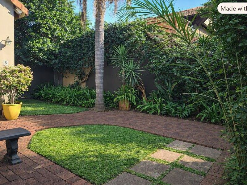 A well-maintained rear garden featuring brick paved pathways, manicured lawn sections, and established perimeter landscaping with a boundary wall.