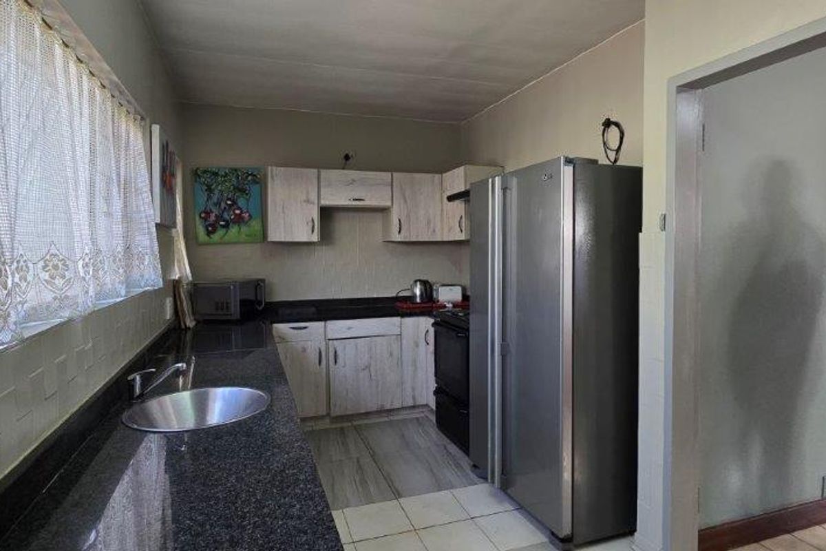 A functional kitchen featuring granite countertops, built-in cabinetry, and tiled flooring, offering a practical layout with space for a large refrigerator.