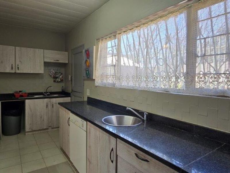 Functional kitchen featuring laminate cabinetry, dark granite countertops, stainless steel sink, and tiled flooring with natural light from large windows.