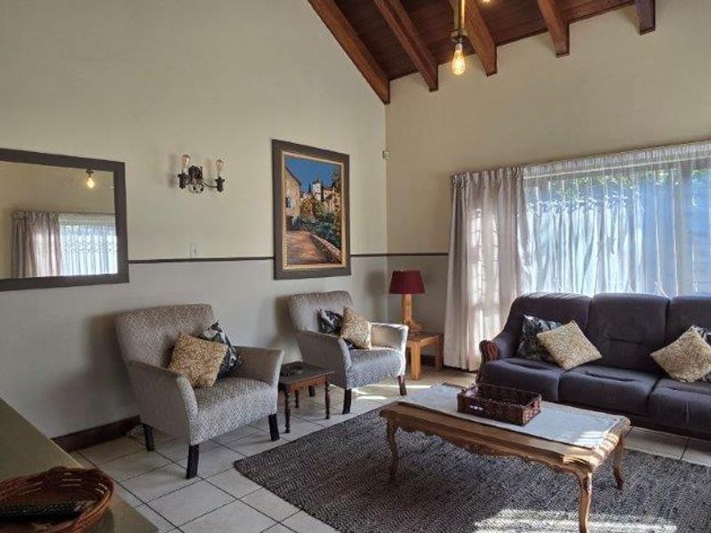 Spacious living room featuring high vaulted ceilings with exposed timber beams, tiled flooring, and large windows allowing for natural light.
