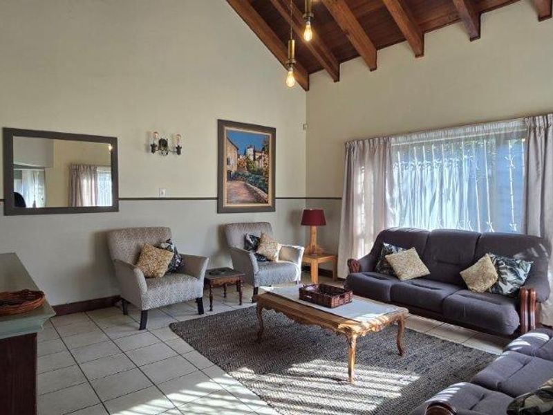 Spacious living room featuring a high vaulted timber ceiling with exposed beams and neutral ceramic floor tiles.