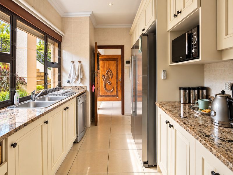 A well-maintained galley kitchen featuring granite countertops, tiled flooring, built-in microwave, and ample cabinetry, leading to a decorative timber door.
