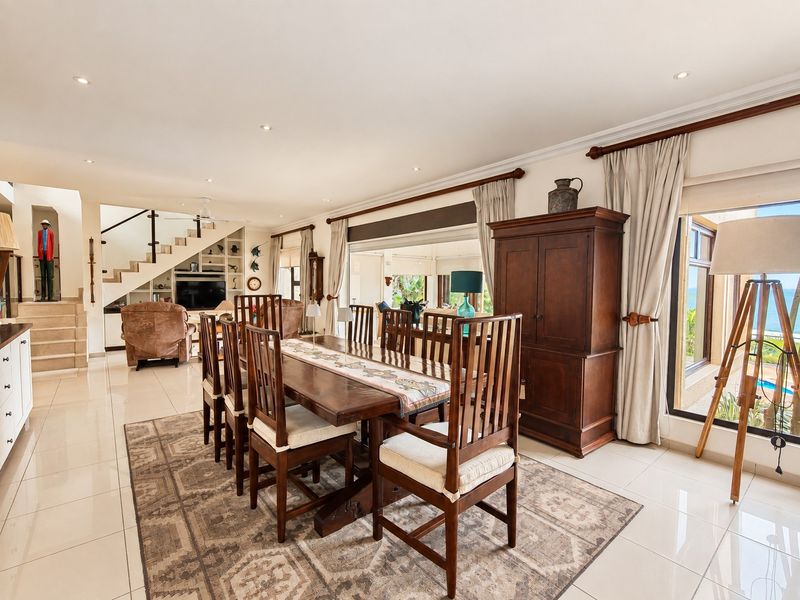Spacious open-plan dining and living area featuring tiled floors, recessed lighting, and a modern staircase with glass balustrade, leading to outdoor access.