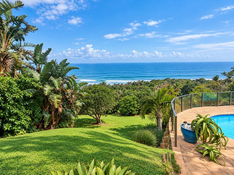 A scenic outdoor pool area featuring a tiled deck, glass balustrade, and expansive views of the lush garden and ocean horizon.