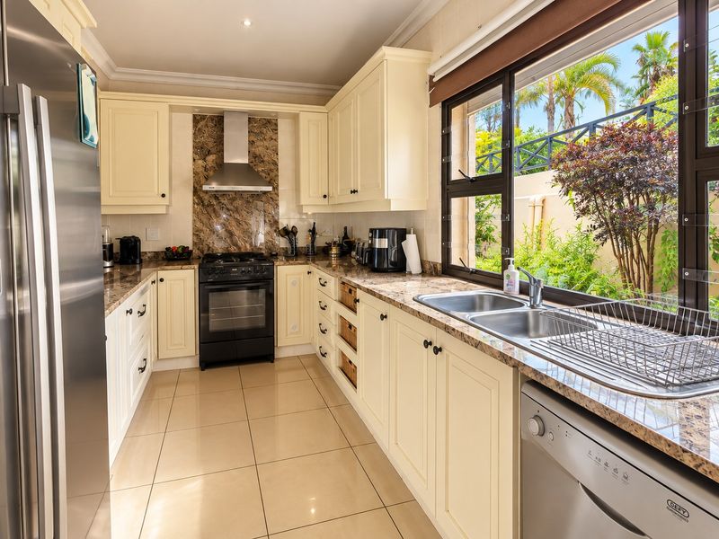 A well-maintained kitchen featuring cream cabinetry, granite countertops, a gas stove with extractor, and large windows overlooking the garden.