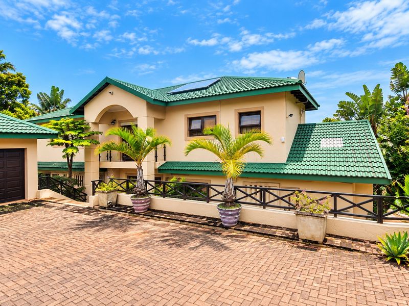 A well-maintained double-story residence featuring a green tiled roof, solar panels, a paved driveway, and a covered balcony entrance.