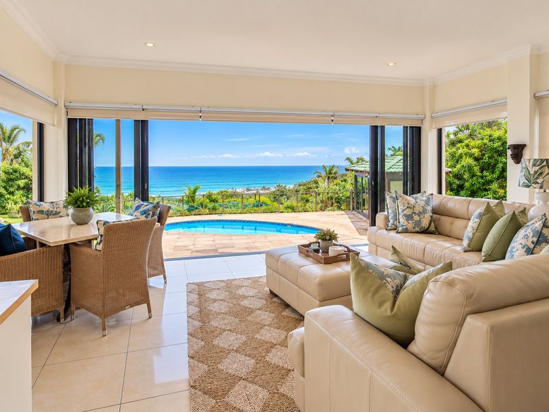 Spacious open-plan living area featuring large bi-fold doors that open onto a patio with a swimming pool and panoramic ocean views.