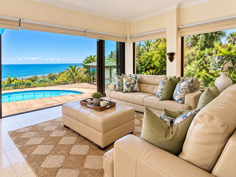 Bright living room featuring large sliding glass doors that open to a patio, swimming pool, and expansive ocean views.
