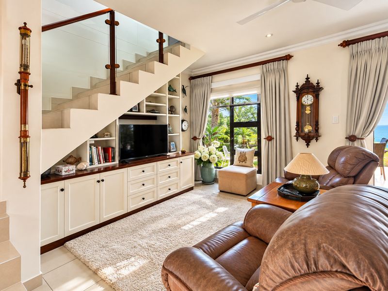 A well-maintained living room featuring custom built-in cabinetry under a staircase, tiled flooring, and large windows with garden and ocean views.