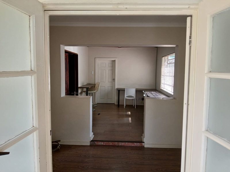 A functional office space featuring laminate flooring, a built-in desk area, and natural light through a window with fitted blinds.