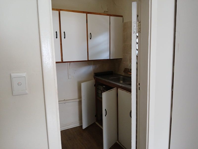A small, dated scullery or utility area featuring built-in cabinetry, a stainless steel sink, and tiled splashback, requiring cosmetic updates.