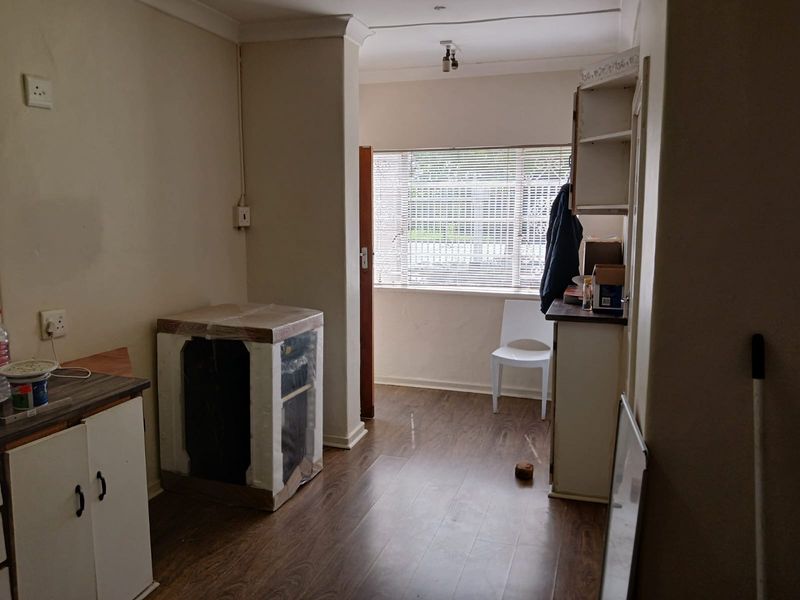 A functional kitchen area featuring laminate flooring, built-in cabinetry, and natural light through a window with venetian blinds.