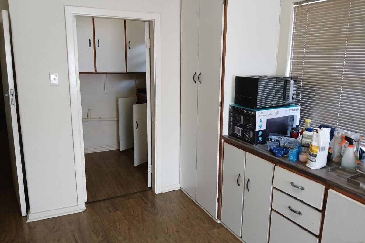 A functional kitchen area featuring built-in cabinetry, laminate flooring, and a separate scullery or pantry space, offering potential for modernization.