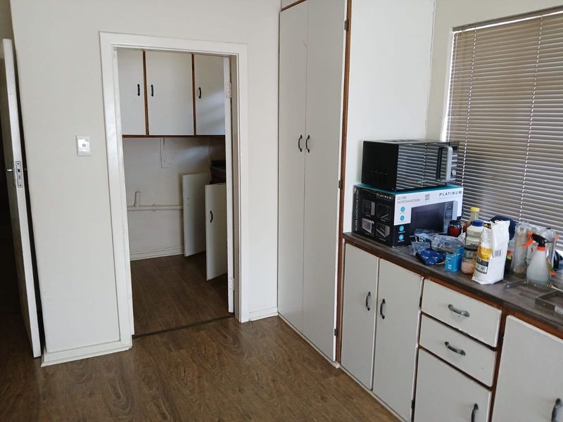 A functional kitchen area featuring built-in cabinetry, laminate flooring, and a separate scullery or pantry space, offering potential for modernization.