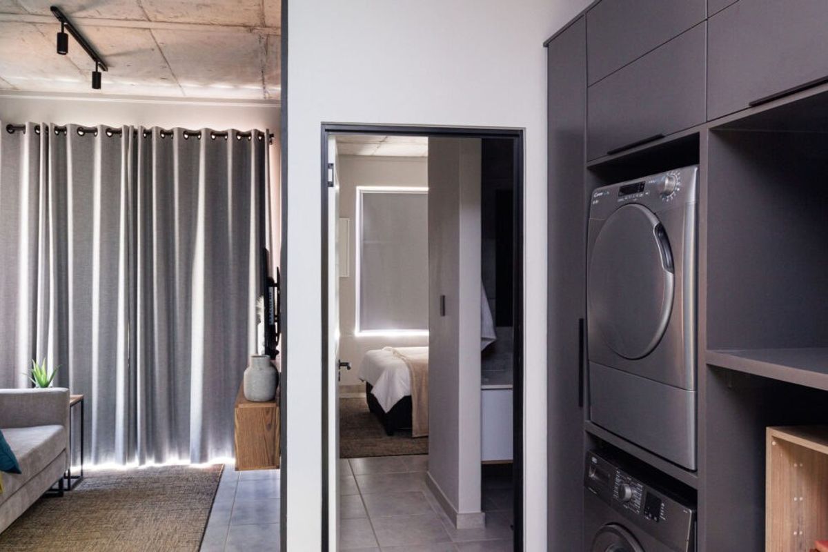 A modern laundry area featuring sleek built-in cabinetry and stacked appliances, with tiled floors and an exposed concrete ceiling.