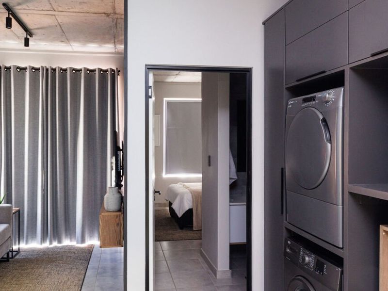 A modern laundry area featuring sleek built-in cabinetry and stacked appliances, with tiled floors and an exposed concrete ceiling.