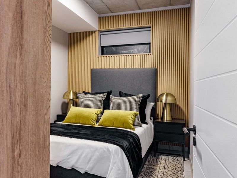 Modern bedroom featuring stylish slatted timber wall paneling, an exposed concrete ceiling, and a high-level window for natural light.
