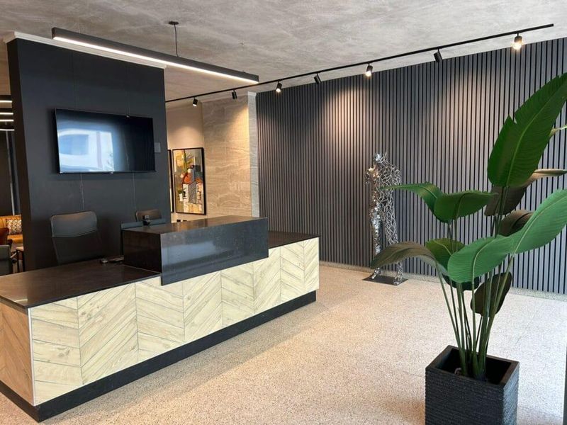 Modern apartment building lobby featuring a custom reception desk, stylish slatted wall paneling, and high-quality terrazzo flooring with contemporary track lighting.