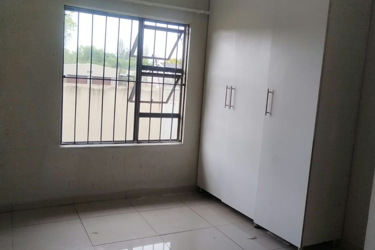 A simple, empty bedroom featuring tiled flooring, a built-in wardrobe, and a window fitted with security bars.