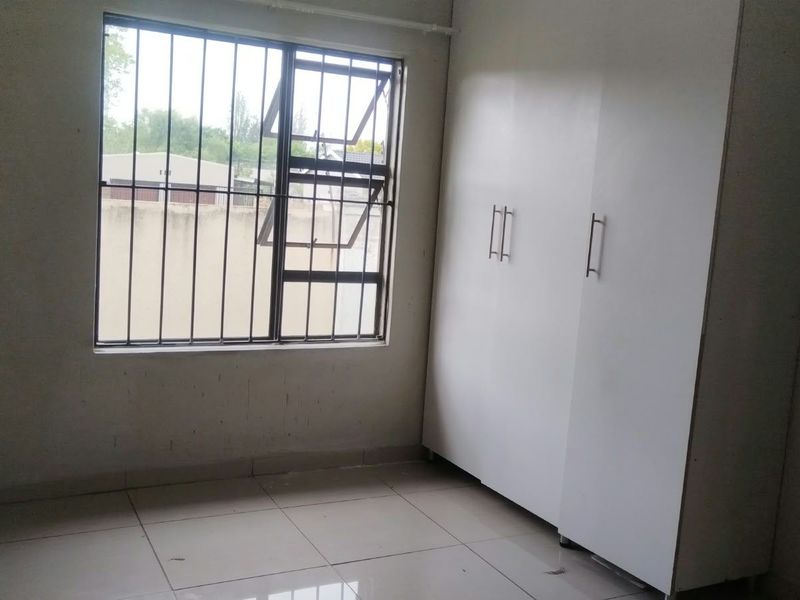 A simple, empty bedroom featuring tiled flooring, a built-in wardrobe, and a window fitted with security bars.