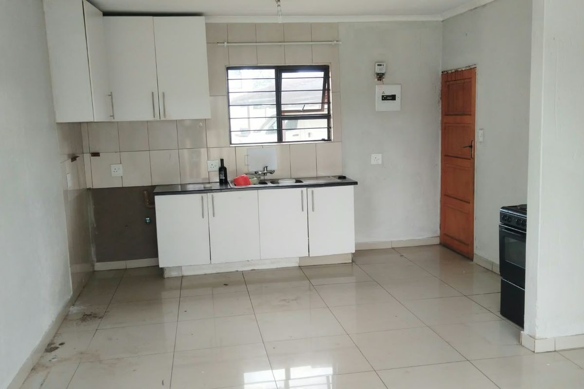 A functional kitchen area featuring white built-in cabinetry, tiled splashbacks, and tiled flooring, requiring some cosmetic updates to reach its full potential.