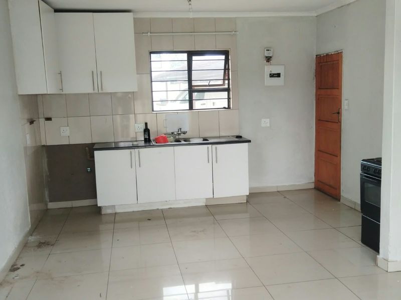 A functional kitchen area featuring white built-in cabinetry, tiled splashbacks, and tiled flooring, requiring some cosmetic updates to reach its full potential.