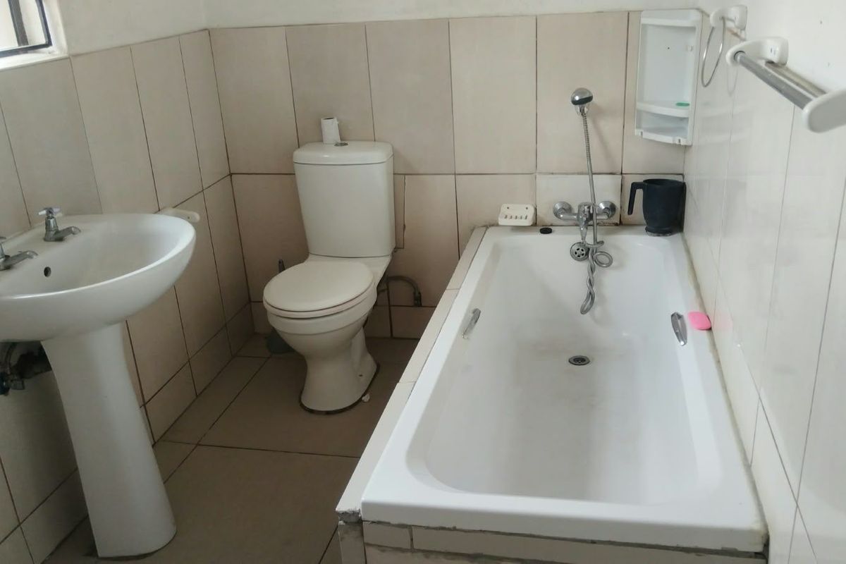 A functional bathroom featuring a pedestal basin, standard toilet, and a built-in bathtub with a handheld shower mixer, finished with neutral ceramic tiling.