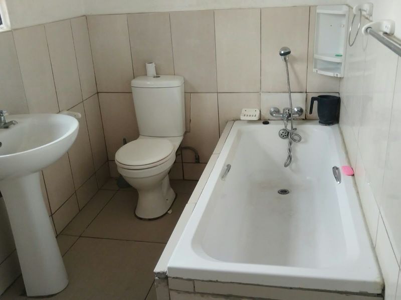 A functional bathroom featuring a pedestal basin, standard toilet, and a built-in bathtub with a handheld shower mixer, finished with neutral ceramic tiling.