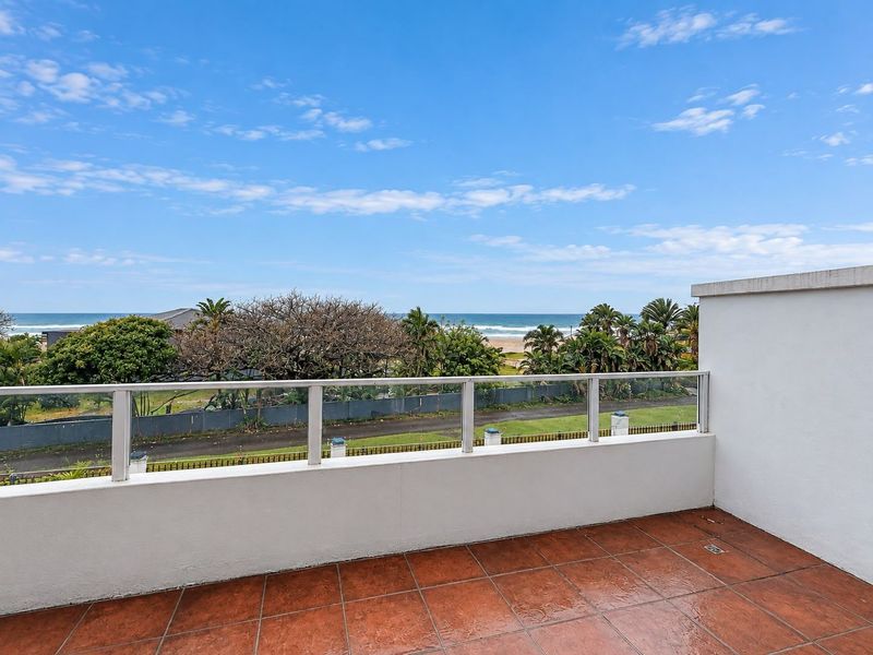 Spacious balcony featuring tiled flooring and a modern glass balustrade, offering clear views of the surrounding landscape and ocean.