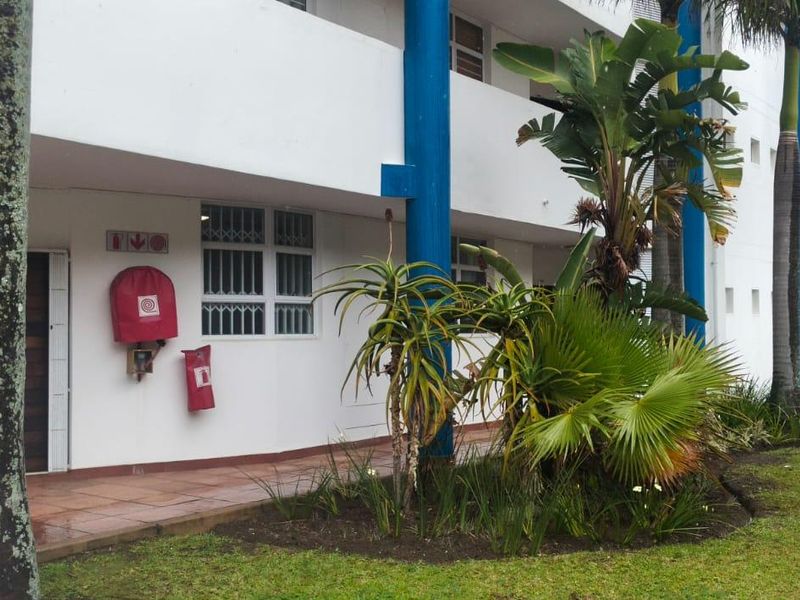 Exterior view of the apartment building entrance featuring a tiled walkway, security bars on windows, and installed fire safety equipment.