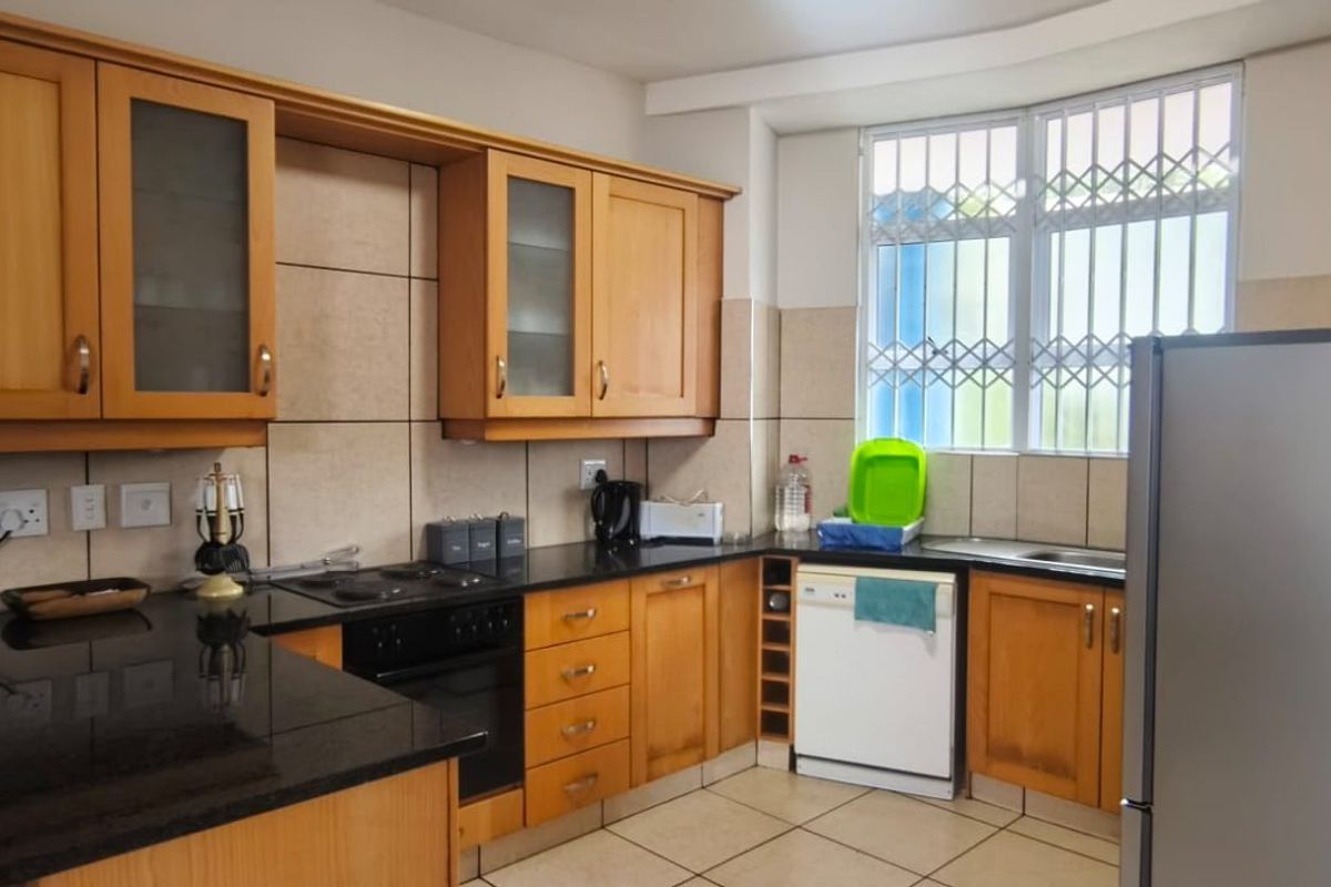 A functional kitchen featuring wooden cabinetry, granite countertops, built-in oven, electric hob, and tiled finishes, offering a practical layout for daily use.