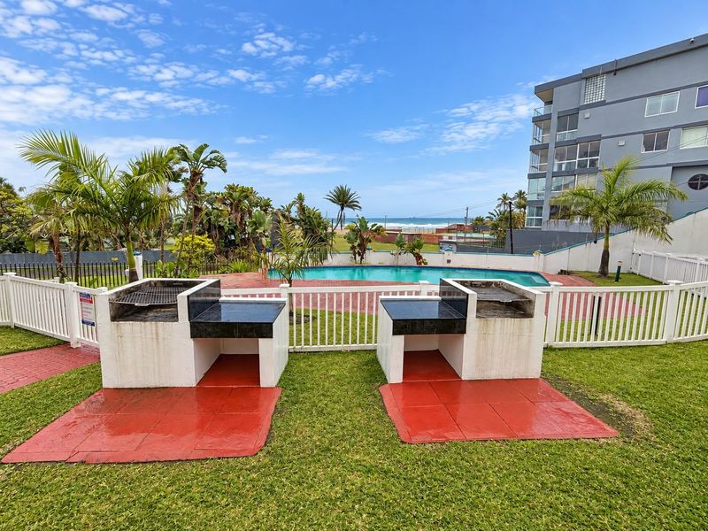 Communal outdoor area featuring a swimming pool, built-in braai stations, and paved surrounds with ocean views.
