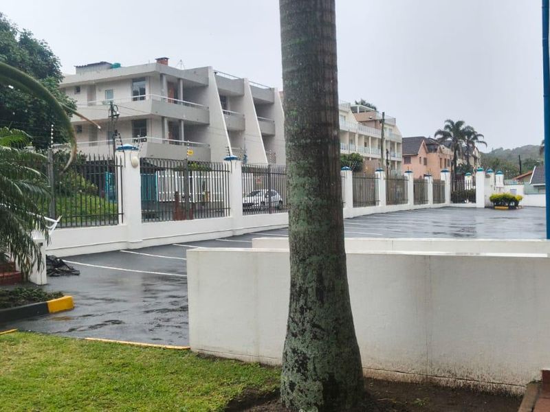 Exterior view of the apartment complex featuring a paved driveway, secure perimeter fencing, and well-maintained garden areas.