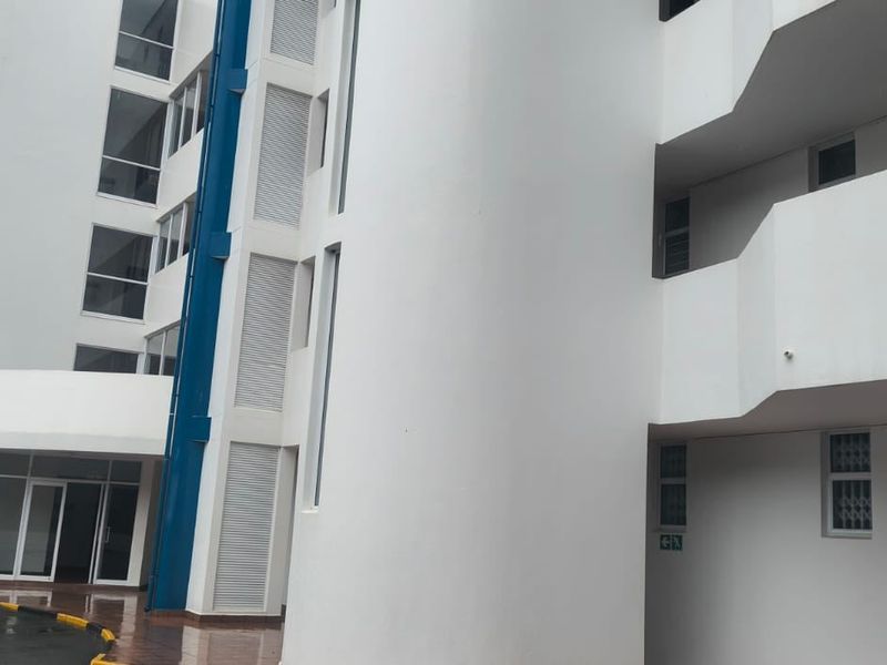 Exterior view of a multi-story apartment building featuring white facade, blue structural accents, and integrated balconies.