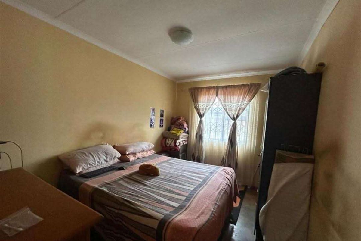 A standard bedroom featuring a window with curtains and basic ceiling lighting, requiring cosmetic updates to the wall finishes.