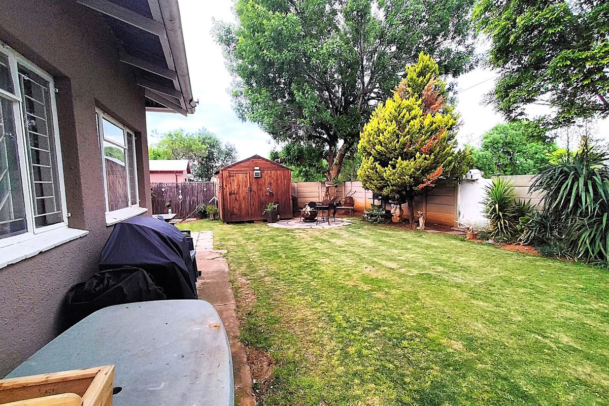 A spacious rear garden featuring a well-maintained lawn, a paved patio area, and a detached wooden storage shed enclosed by precast concrete boundary walls.