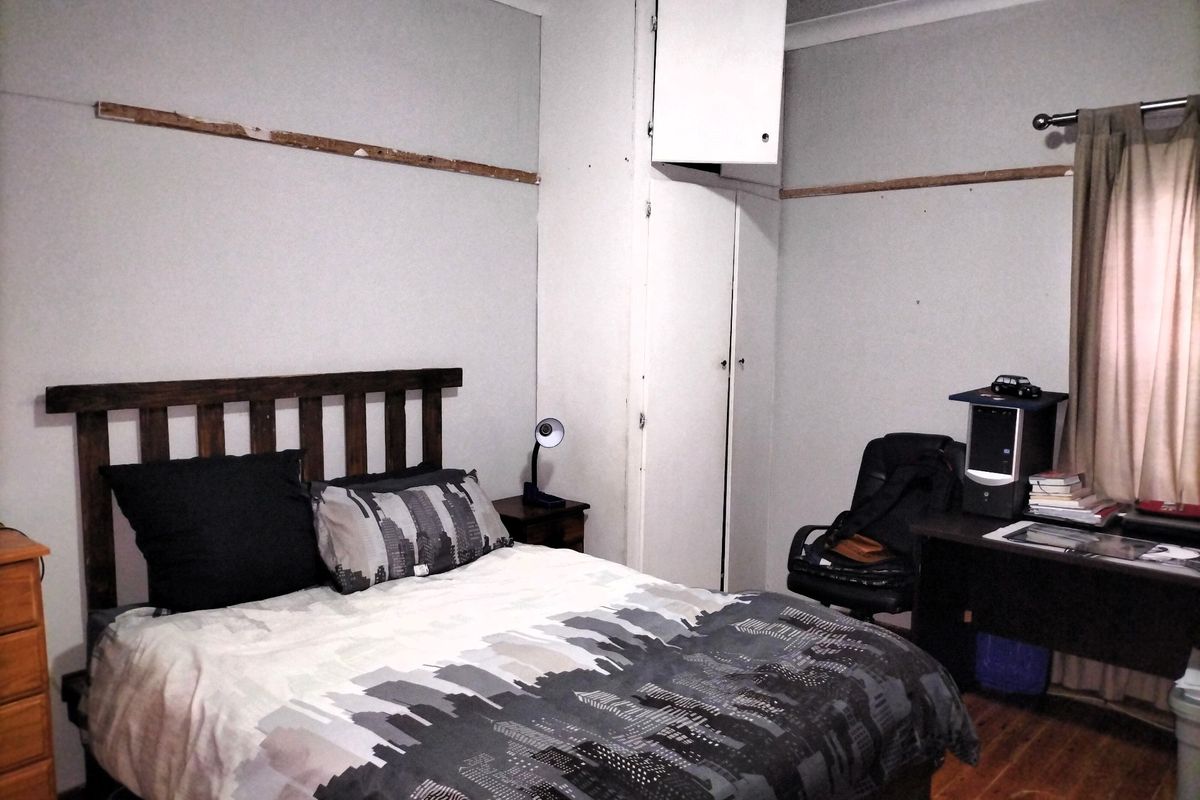 A bedroom featuring timber flooring, built-in wardrobe storage, and coving. The room requires cosmetic updates to the wall finishes and trim.