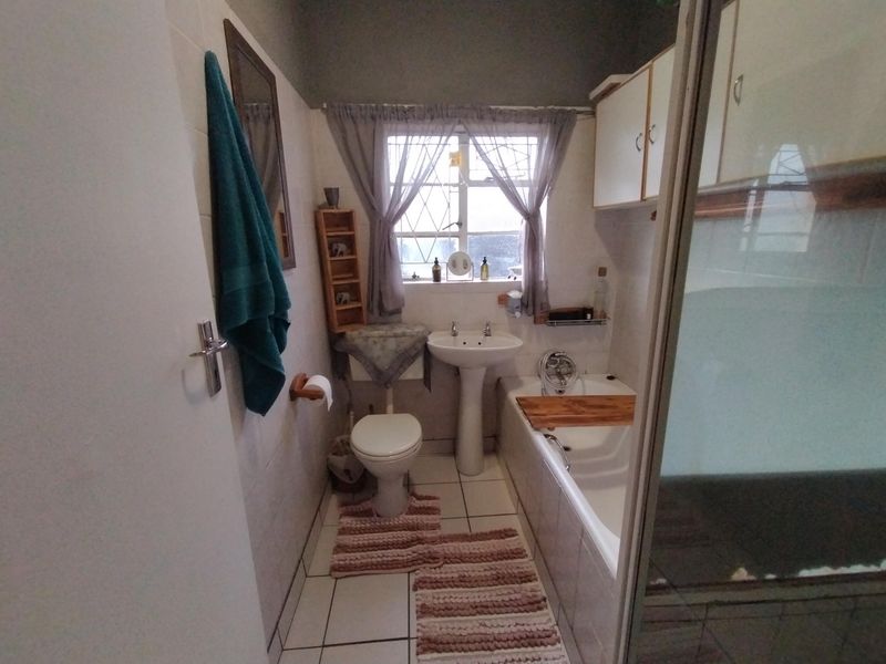 A functional bathroom featuring a pedestal basin, toilet, and bathtub with wall-mounted storage cabinetry and tiled flooring.