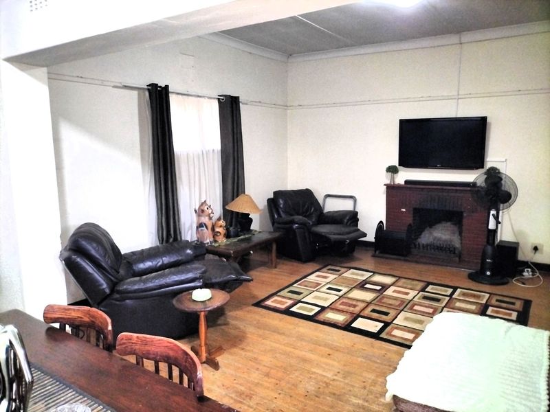 A living room featuring a brick fireplace and hardwood flooring, requiring cosmetic updates to improve the overall aesthetic and condition of the space.
