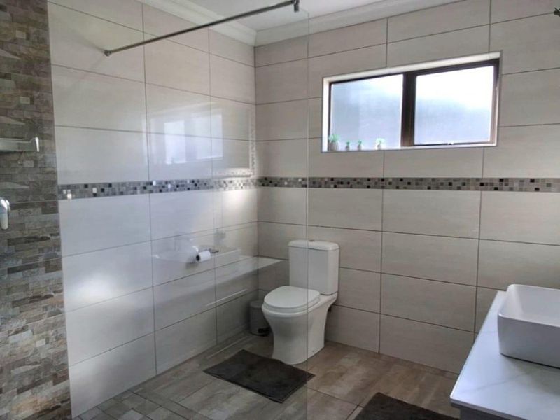 Modern bathroom featuring a glass shower screen, neutral ceramic wall tiles with a mosaic accent, a vessel sink vanity, and a toilet.