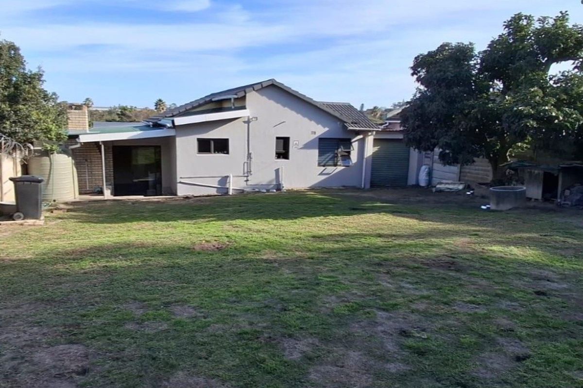 Rear view of the property featuring a spacious garden, covered patio area, water tank, and attached garage access.