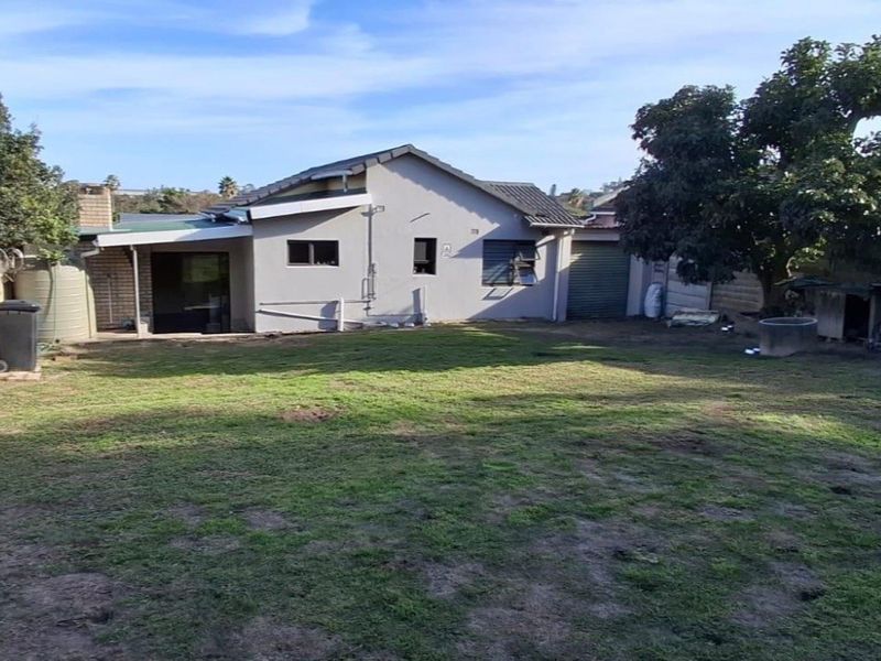 Rear view of the property featuring a spacious garden, covered patio area, water tank, and attached garage access.